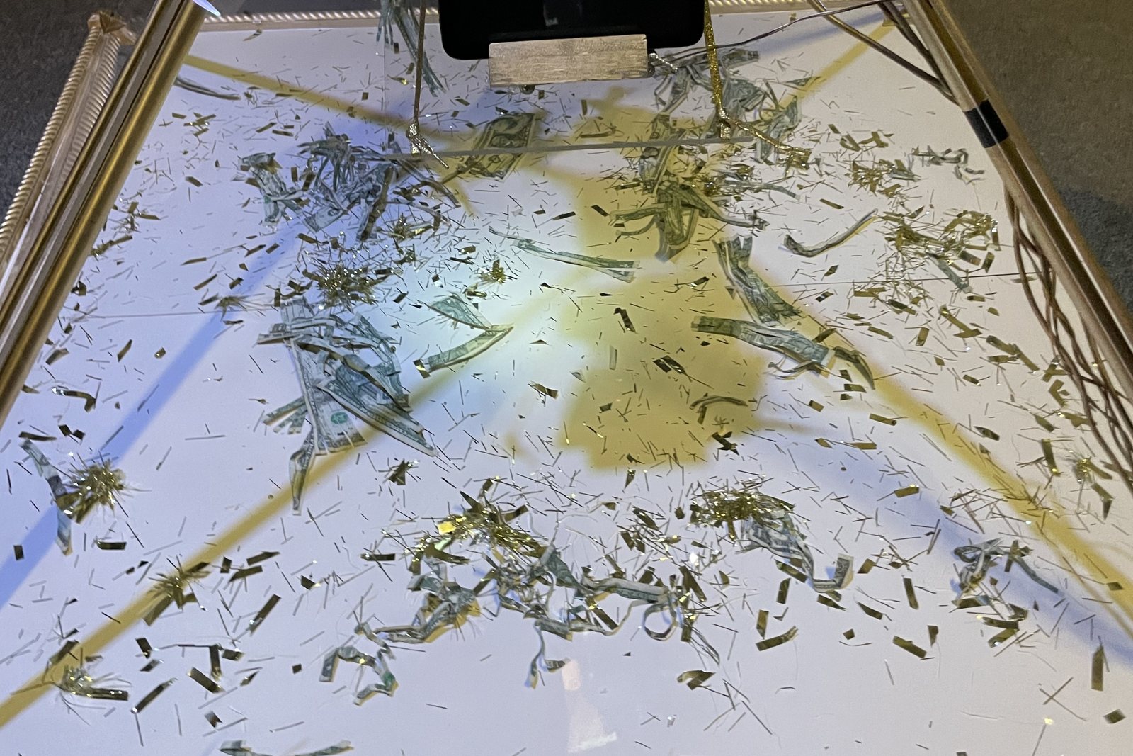 Looking down into the pyramid at the white lit platform, covered in shredded banknotes with recognisable fragments of dollar bills among the confetti