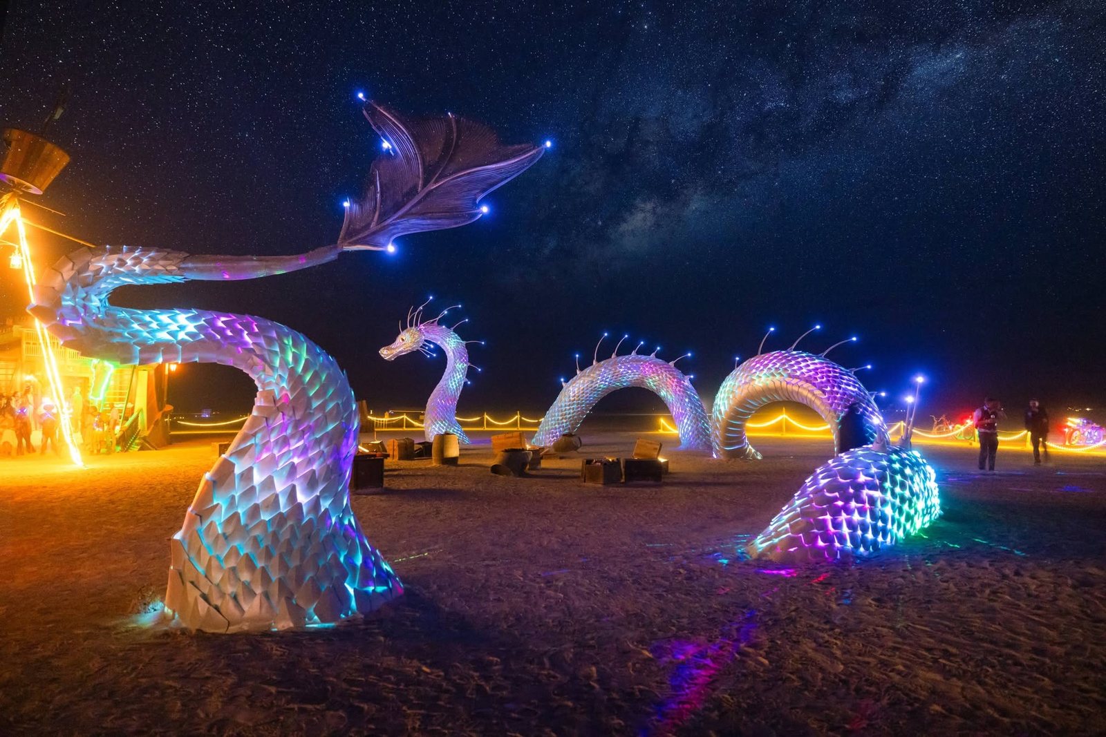 The whole serpent lit at night under the Milky Way: body glowing through the scales and bright points of color along the spine