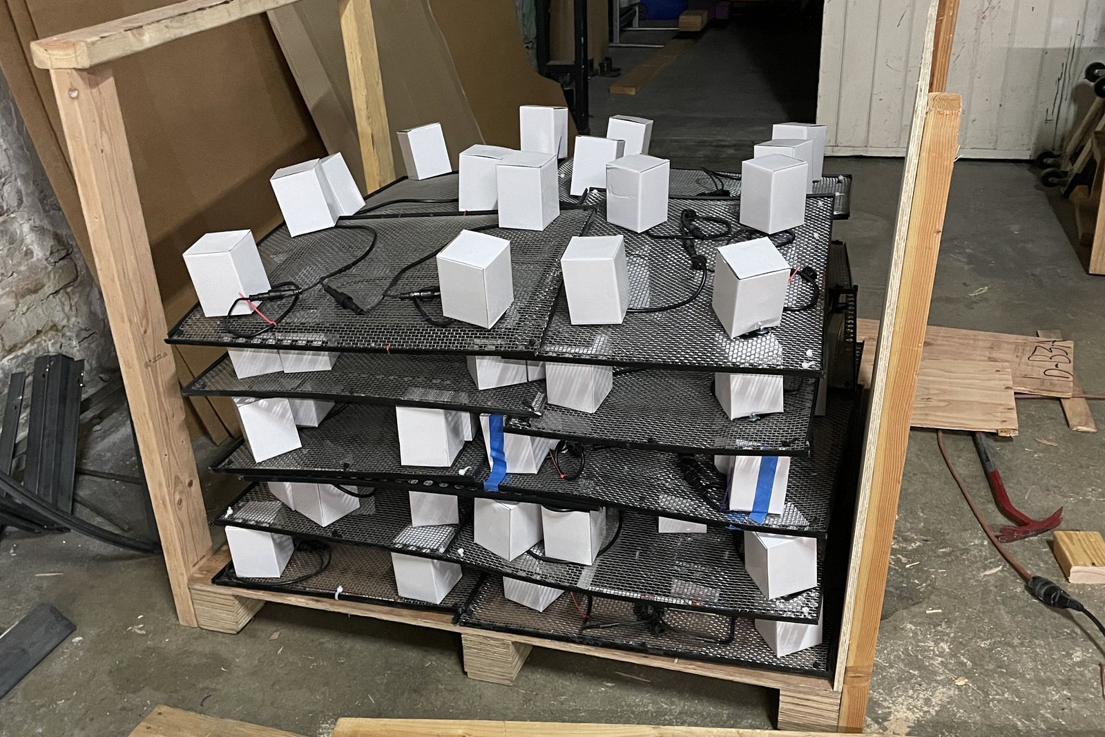 Mesh panels stacked in a wooden crate, each one carrying a row of white diffuser boxes over its spotlights, ready to ship