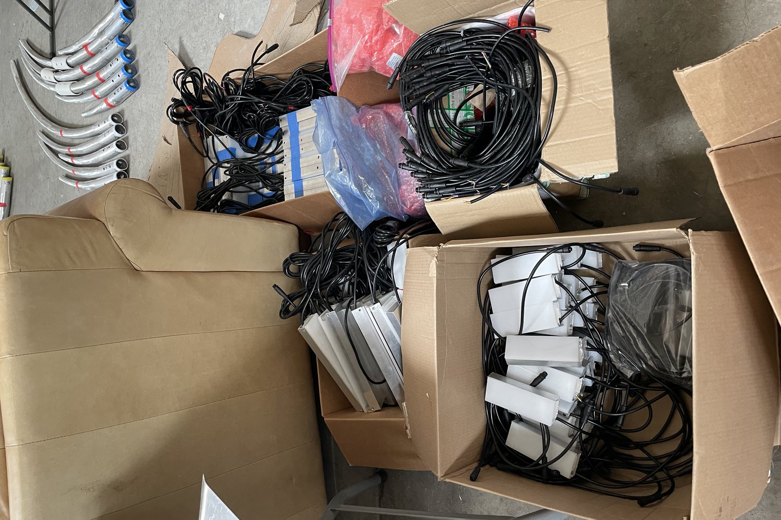 Finished parts laid out on a workshop floor: spikes with colored tape markings, white aluminum frames, and coils of wire harness in open boxes