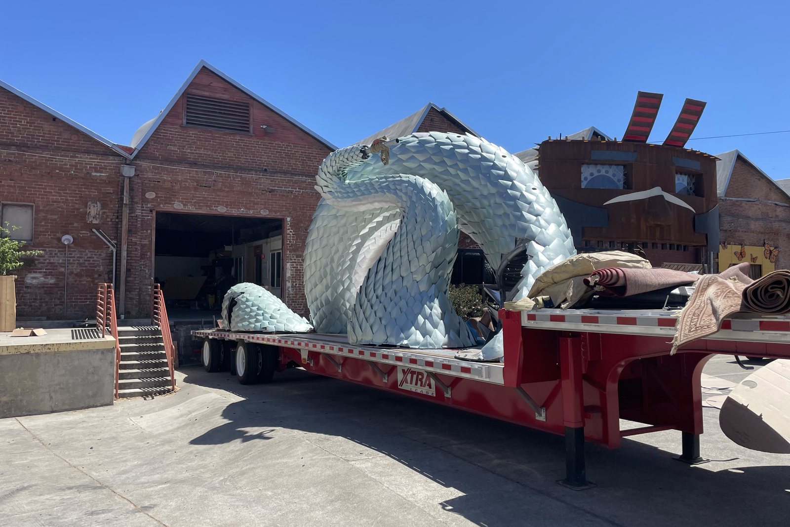 A hump section of the serpent on a red flatbed trailer in daylight, its overlapping pale scales covering the steel mesh underneath