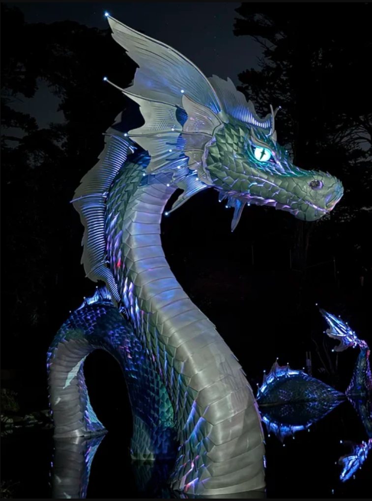 Naga's head and neck at night, scales washed blue and violet from inside, one eye glowing, spike pixels bright along the fins