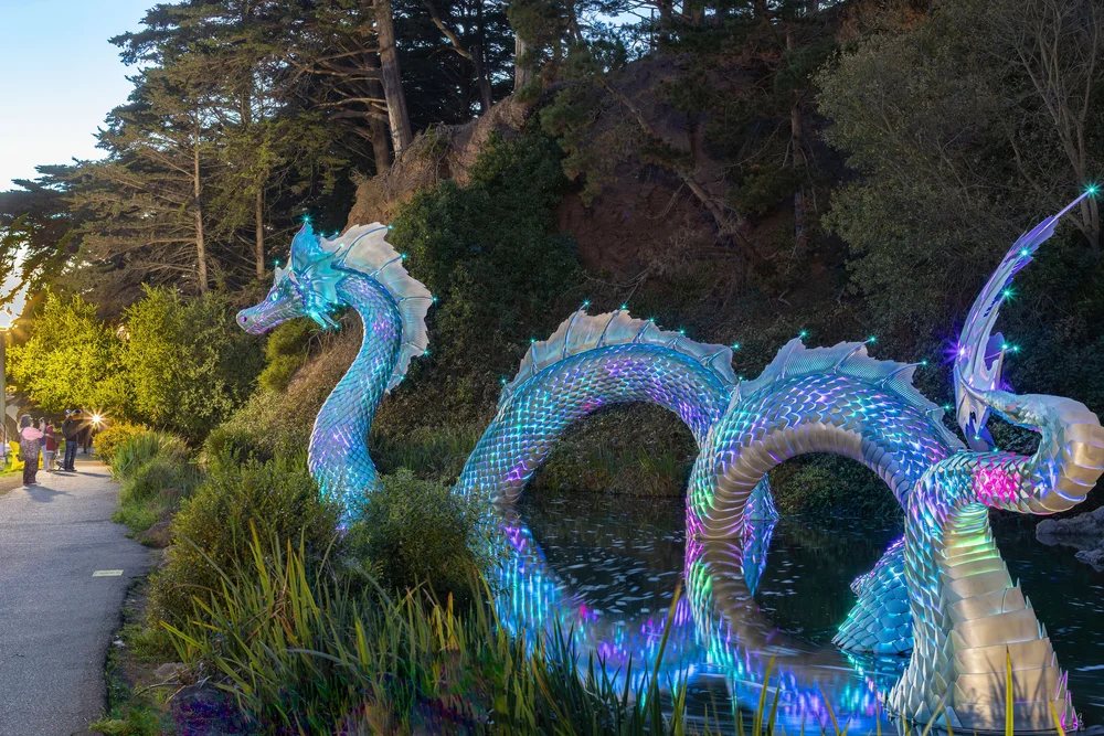 Naga lit in blue and violet, curving over the pond in Golden Gate Park at dusk